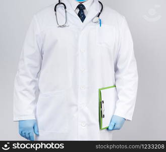 male doctor in a white coat, blue latex gloves, a stethoscope hanging on his neck, doctor holding a green paper holder with a white blank sheet