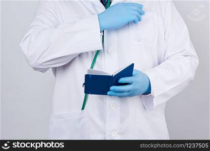 male doctor in a white coat with buttons, wearing blue sterile gloves, holding a open blue paper notebook in his hand on a white studio background