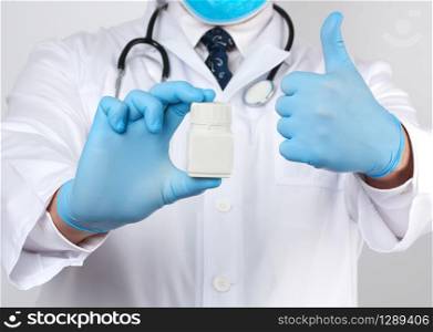 male doctor in a white medical coat and blue latex gloves holds a white plastic jar of pills, close up