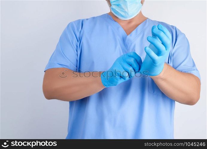 male doctor in blue uniform puts on his hands white sterile latex gloves before surgery, white background