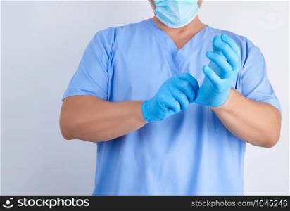 male doctor in blue uniform puts on his hands white sterile latex gloves before surgery, white background