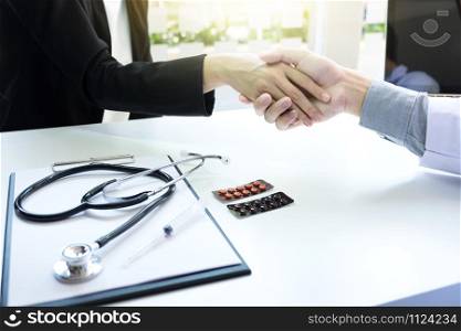 Male doctor in white coat shaking hand to female patient after successful treatment.