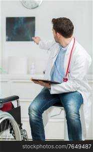 male doctor pointing and showing a scan to disabled patient