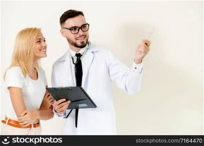 Male doctor points pen at empty copy space while standing beside female patient.. Male doctor with patient points pen at copy space.