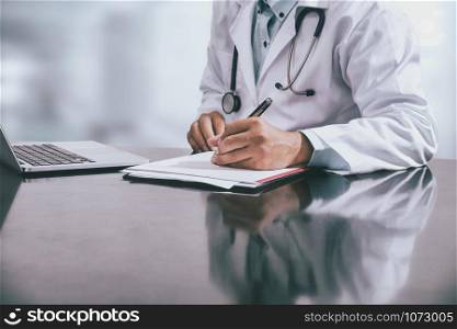 Male doctor sitting at table and writing on a document report in hospital office. Medical healthcare staff and doctor service.