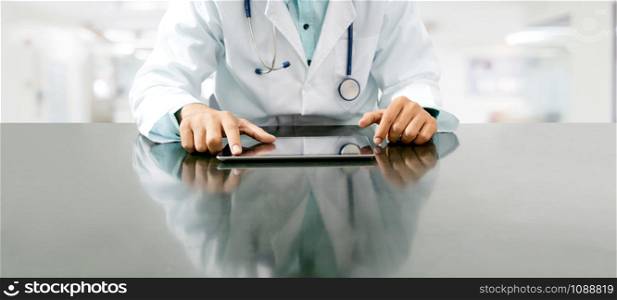 Male doctor sitting at table with tablet computer in hospital office. Medical healthcare staff and doctor service.