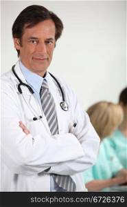 Male doctor stood with arms folded colleagues in background
