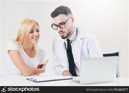 Male doctor talks to female patient in hospital office while looking at the patients health data on laptop computer on the table. Healthcare and medical service.