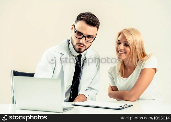 Male doctor talks to female patient in hospital office while looking at the patients health data on laptop computer on the table. Healthcare and medical service.