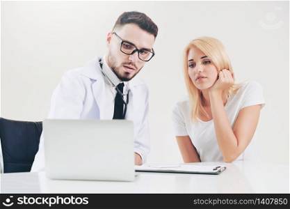 Male doctor talks to female patient in hospital office while looking at the patients health data on laptop computer on the table. Healthcare and medical service.. Male Doctor and Female Patient in Hospital Office