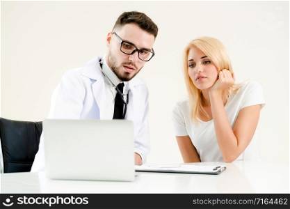 Male doctor talks to female patient in hospital office while looking at the patients health data on laptop computer on the table. Healthcare and medical service.. Male Doctor and Female Patient in Hospital Office