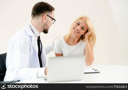 Male doctor talks to female patient in hospital office while looking at the patients health data on laptop computer on the table. Healthcare and medical service.. Male Doctor and Female Patient in Hospital Office