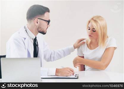 Male doctor talks to female patient in hospital office while writing on the patients health record on the table. Healthcare and medical service.
