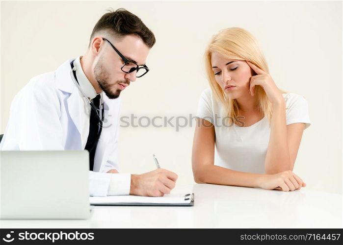 Male doctor talks to female patient in hospital office while writing on the patients health record on the table. Healthcare and medical service.. Male Doctor and Female Patient in Hospital Office