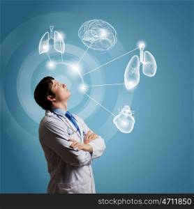 Male doctor thinking. Young concentrated male doctor with arms crossed against digital background