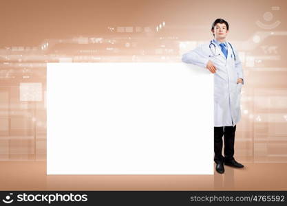 Male doctor with banner. Young male doctor leaning upon blank banner. Place for text