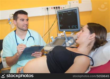 male doctor writing notes while pregnant woman lying on bed