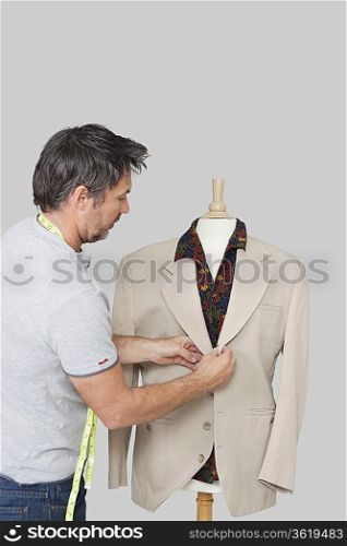 Male dressmaker adjusting suit on tailor&acute;s dummy over colored background