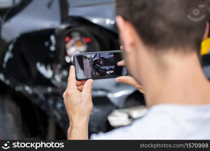 Male Driver Taking Photo Of Damaged Car After Accident For Insurance Claim On Mobile Phone