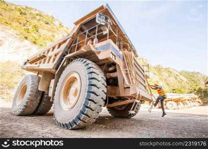 Male driver walks up the stairs of large quarry dump truck at open space, production useful minerals, to transport coal from open pit in mountainous area.