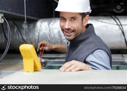male electrician testing roof electronics with multimeter