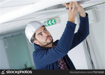 male electrician with screwdriver repairing fire sensor