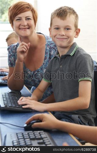 Male Elementary Pupil In Computer Class With Teacher