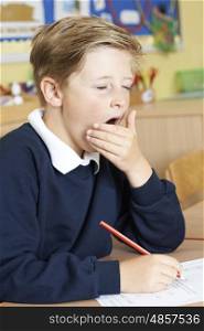 Male Elementary School Pupil Yawning In Classroom