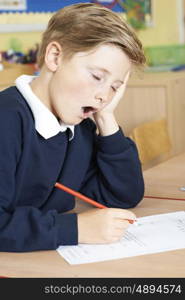 Male Elementary School Pupil Yawning In Classroom