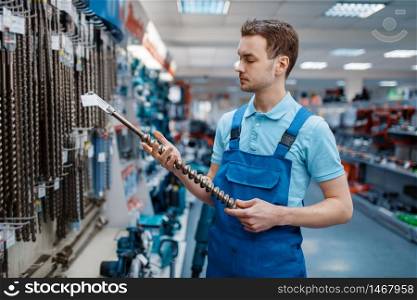 Male employee in uniform choosing concrete drill in tool store. Choice of professional equipment in hardware shop, instrument supermarket. Employee choosing concrete drill in tool store