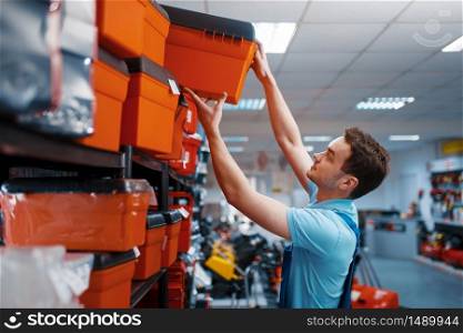 Male employee in uniform choosing toolbox in tool store. Choice of professional equipment in hardware shop, instrument supermarket. Male employee choosing toolbox in tool store