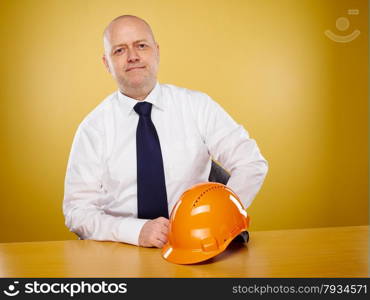 Male engineer in office, he wearing a white shirt and tie, the orange hard hat is on the table