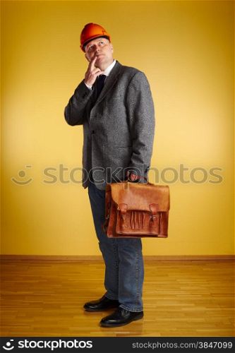 Male engineer, inspect the room and he holds old leather briefcase, parquet floor and yellow wall