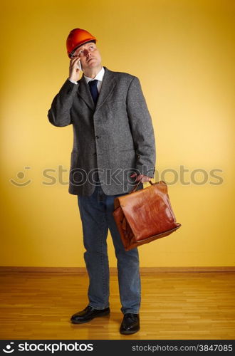 Male engineer, uses cellphone and inspect the room and he holds old leather briefcase, parquet floor and yellow wall