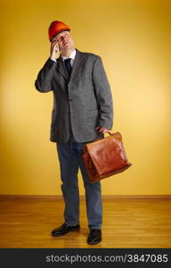 Male engineer, uses cellphone and inspect the room and he holds old leather briefcase, parquet floor and yellow wall