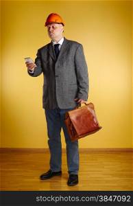 Male engineer, uses cellphone and inspect the room and he holds old leather briefcase, parquet floor and yellow wall