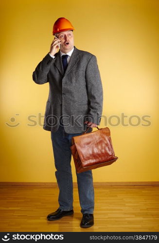 Male engineer, uses cellphone and inspect the room and he holds old leather briefcase, parquet floor and yellow wall