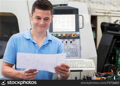 Male Engineer With Technical Drawing Operating CNC Machine In Factory
