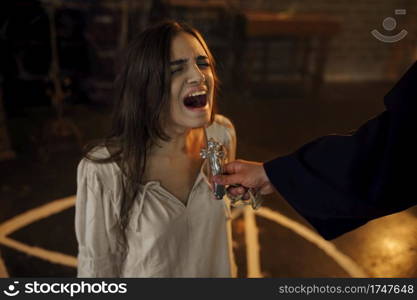 Male exorcist in black hood casting out devil from scary woman. Exorcism, mystery paranormal ritual, dark religion, night horror. Exorcist casting out devil from scary woman