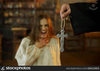 Male exorcist in black hood casting out devil from scary woman. Exorcism, mystery paranormal ritual, dark religion, night horror, potions on shelf on background. Exorcist casting out devil from scary woman