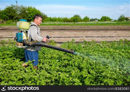 Male farmer with a mist sprayer processes potato bushes with chemicals. Control of use of chemicals. Farming growing vegetables. Protection of cultivated plants from insects and fungal infections.
