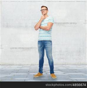 male, fashion and people concept - smiling young man in eyeglasses thinking over stone wall background