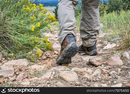 male feet in hiking leather boots on a rocky mountain uphill trail
