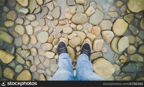 Male feet in sneakers standing on riverbank covered with pebbles