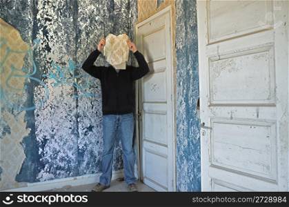 Male figure obscured by torn wallpaper shred in abandoned house interior.
