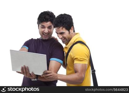 Male friends laughing while using laptop