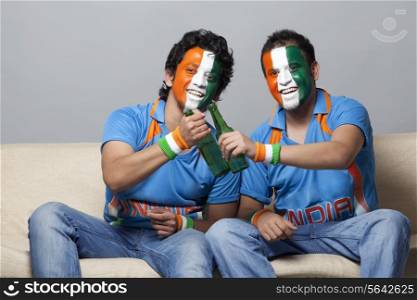 Male friends with painted face in tricolor bottle while sitting together on sofa