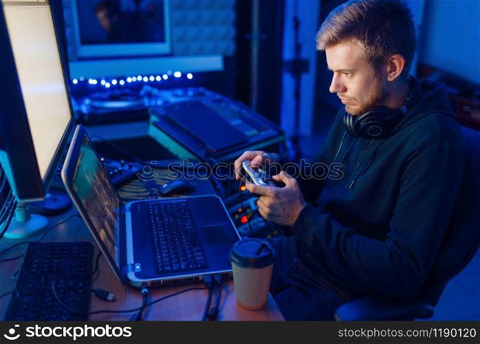 Male gamer in headphones holds joystick and playing videogame on console or desktop PC, gaming lifestyle, cybersport. Computer games player in his room with neon light, streamer. Gamer with joystick playing videogame on console