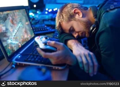 Male gamer with joystick in hands sleeping at his laptop after challenge, gaming lifestyle, cybersport. Online multiplayer computer games, consol videogame, player in his room with neon light