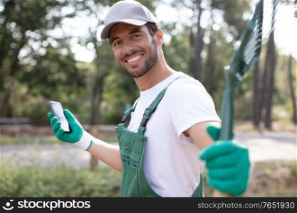 male gardener holding a rake and a smartphone